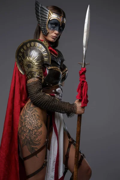 拍摄的女战士与油漆脸身穿盔甲和红色斗篷灰色背景 — 图库照片