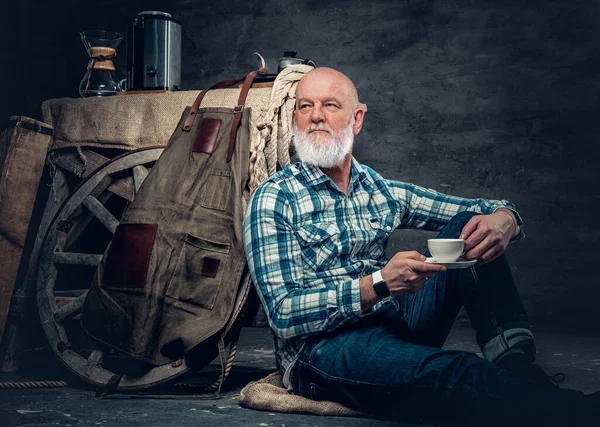 Portrait of senior barista sitting on floor around his old fashioned mobile coffee shop.