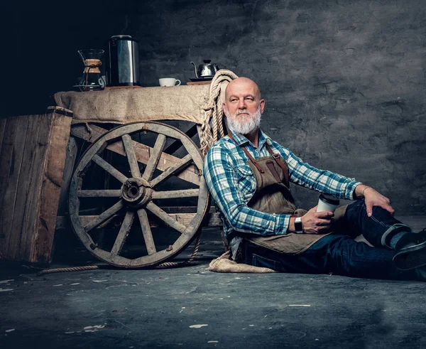 Portrait of senior barista sitting on floor around his old fashioned mobile coffee shop.