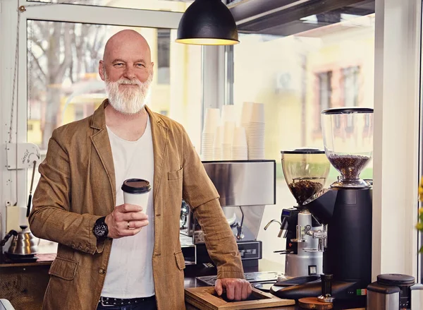 stock image Shot of glad elderly barman with coffee cup posing in coffee shop in daytime.