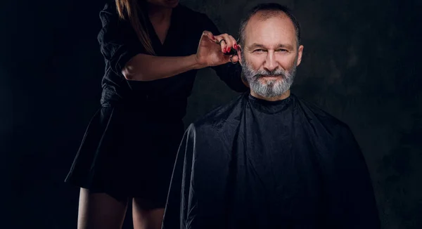 Studio shot of professional woman barber with scissor and her elderly customer.