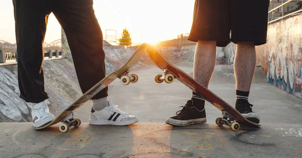 Portrait of two tattooed hipster boys with skateboards at skatepark at sunset.