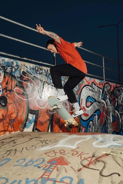Portrait of hipster boy showing tricks on skateboard at skatepark with graffiti walls.