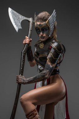 Zırhlı vahşi Valkyrie 'nin portresi. Elinde kocaman bir baltayla gri arka planda kameraya bakıyor..