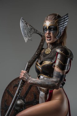 Zırhlı öfkeli Valkyrie 'nin portresi. Elinde kocaman bir baltayla gri arka planda kameraya bakıyor..