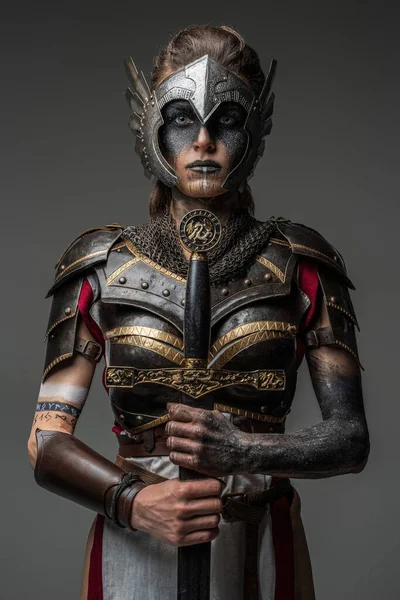 Antique female knight dressed in steel armor holding sword against dark background.