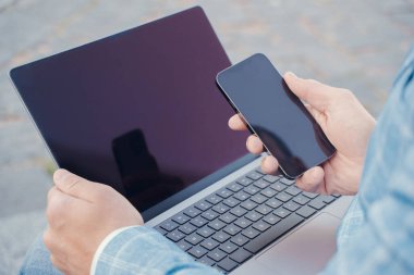 Connection of cellphone and laptop. Businessman dressed in suit holding laptop and cellphone.