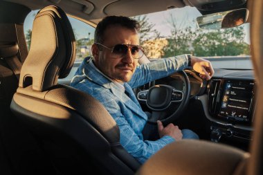 Portrait of stylish business man with sunglasses looking at camera inside his expensive automobile.
