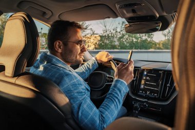 Shot of business man using mobile phone sitting inside his luxurious car in city.