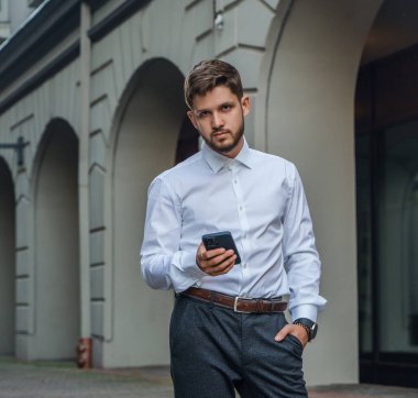 Shot of busy man dressed in formal clothes using his cellphone walking around city.