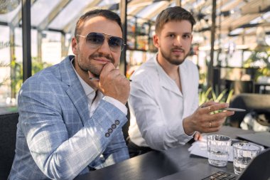 Shot of professional two businessmen working with laptop looking at camera in office.