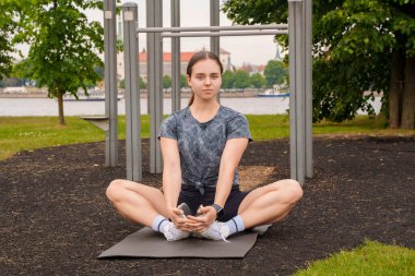 Portrait of active female athlete doing yoga training on sports ground in summertime outdoors.
