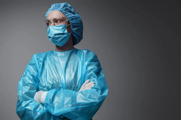 Shot of surgeon woman with crossed arms dressed in modern surgical uniform against grey background.
