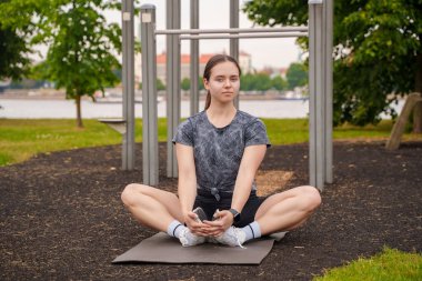 Portrait of active female athlete doing yoga training on sports ground in summertime outdoors.
