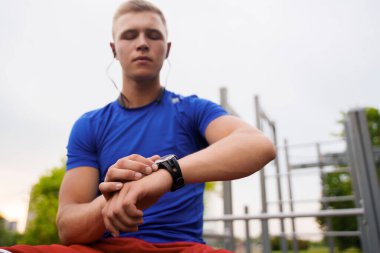 Shot of blond haired athlete dressed in sportswear setting timer on his watch outdoors in city.