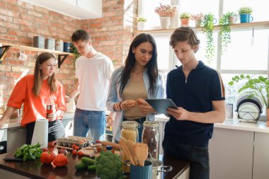 Shot of guy with tablet looking for recipe in internet around his three friends in kitchen.