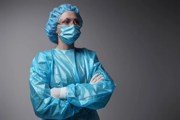 Shot of surgeon woman with crossed arms dressed in modern surgical uniform against grey background.