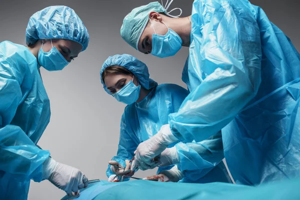 Portrait Three Surgeons Dressed Surgical Uniform Treating Injured Patient Grey — 图库照片
