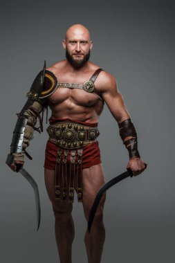 Portrait of ancient gladiator dressed in armour holding swords isolated on gray.