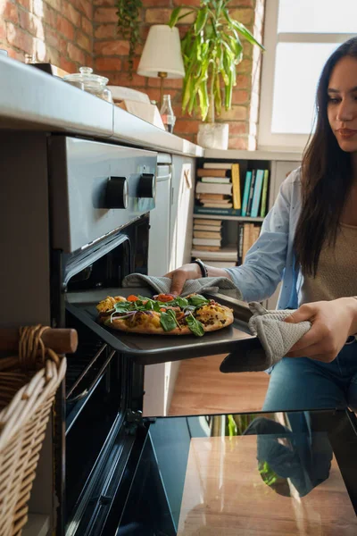 Shot of woman dressed in casual attire baking home made pizza for her friends.