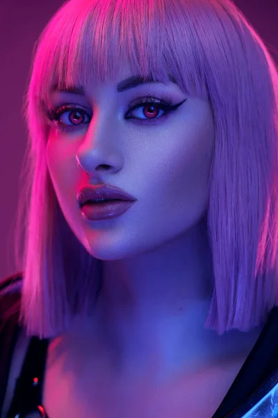 Headshot of cyberpunk woman with lenses and short hairs looking at camera against pink background.