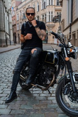 Sokakta motosikletine dövme yaptırmış çekici bir motorcunun portresi..