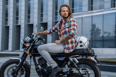 Şehir caddesinde uzun saçlı, havalı maço bir motosikletin portresi..