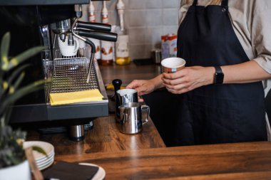 Önlüklü kadın barmen kahve dükkanında kahveye süt hazırlarken..