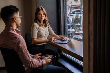 Bilgisayarlı kadın ve erkeğin kahve dükkanında gevşeyip konuştuğu bir fotoğraf..