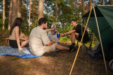 Çay içen ve kampla ormanda yürüyüş yapan dört arkadaşın portresi..
