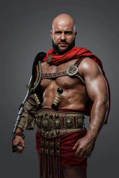Shot of muscular bald man with beard dressed in ancient roman gladiator costume.