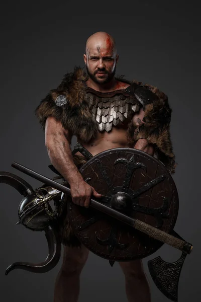 Portrait of nordic warrior with muscular build and horned helmet against gray background.