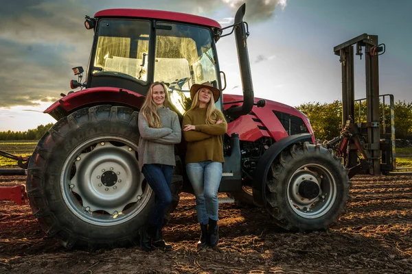 Portrait of female farmers in farm with modern combine on cultivated field.
