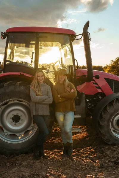Portrait of female farmers in farm with modern combine on cultivated field.