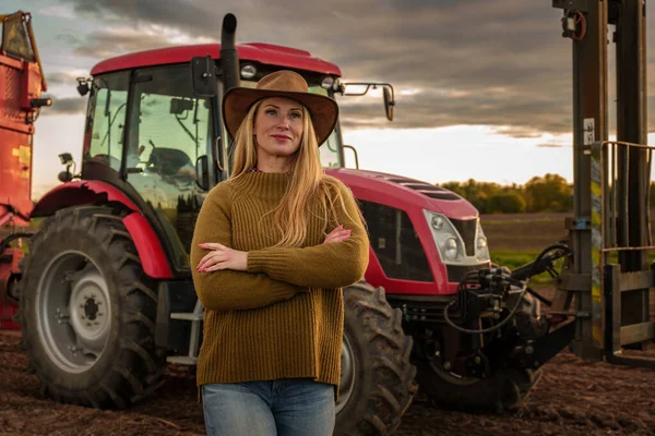 Portrait of confident farmer woman and modern combine on cultivated field.