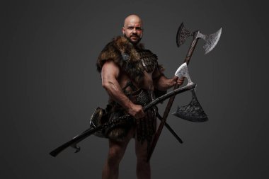 Zırh ve kürk giymiş yakışıklı Viking 'in iki balta tuttuğu bir stüdyo fotoğrafı..