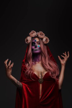 Kırmızı pelerin ve gül çelengi giymiş, makyajlı, korkunç iblis kadın..
