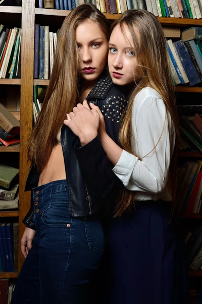 Two beautiul women holding and posing in the library. — Stock Photo, Image