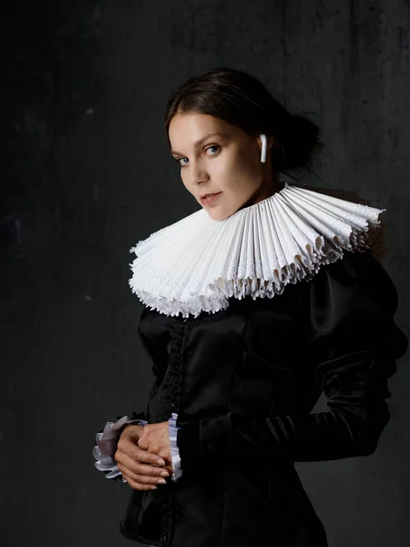 A noble lady in an old round collar enjoys music using modern headphones. — Stock Photo, Image