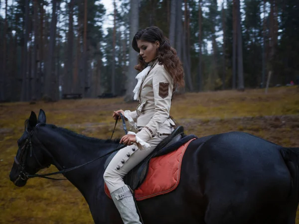 Una joven hermosa jinete morena en un elegante traje retro montando un caballo negro —  Fotos de Stock
