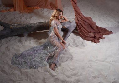 Göz alıcı bir portre. Parlak seksi elbisesiyle kumların üzerinde muhteşem bir genç kadın.