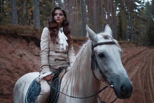Una joven hermosa jinete morena en un elegante traje retro montando un caballo blanco — Foto de Stock
