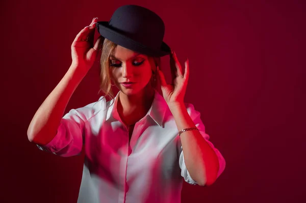 Una joven mujer con estilo en una camisa blanca y un sombrero de boliche negro, estilo estricto, —  Fotos de Stock