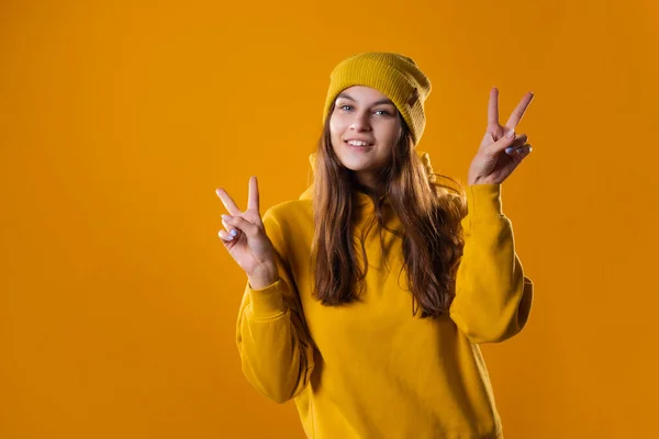 Stylowa młoda brunetka w żółtej bluzie pokazuje gest zwycięstwa — Zdjęcie stockowe