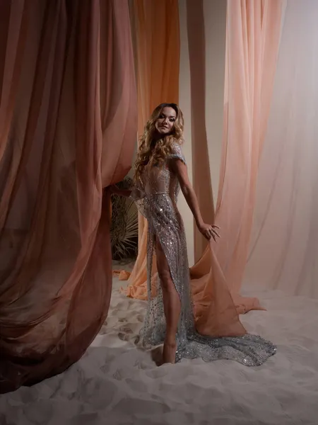 Una joven rubia elegante en un vestido de lujo detrás de una cortina —  Fotos de Stock