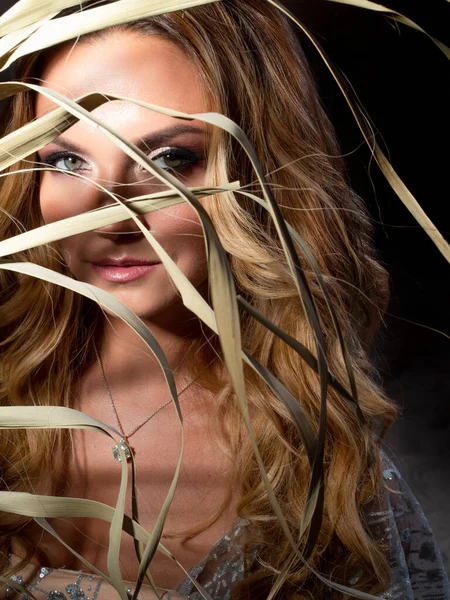 Eine schöne junge Frau mit hellem Make-up versteckt sich im Schatten eines Palmenzweiges. — Stockfoto