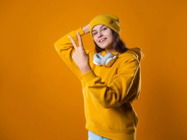 Sarı kapüşonlu hoş, genç esmer kız zafer işareti yapıyor.