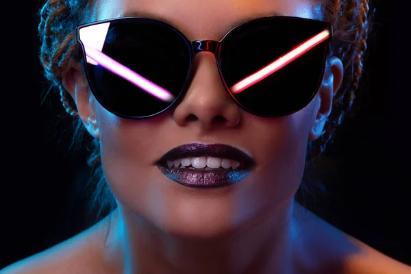 Neon style, reflection of neon lamps in dark glasses of a young stylish woman,