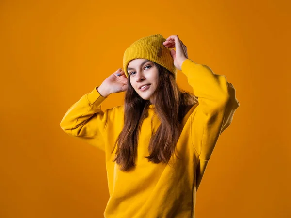 Stijlvolle vrolijke jonge brunette in een gele hoodie en hoed op een geel — Stockfoto
