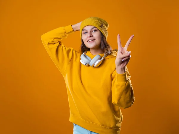 Elegante alegre jovem morena em um capuz amarelo mostra um gesto de vitória — Fotografia de Stock